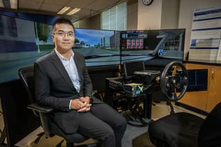 Professor sits in front of a driving simulation setup