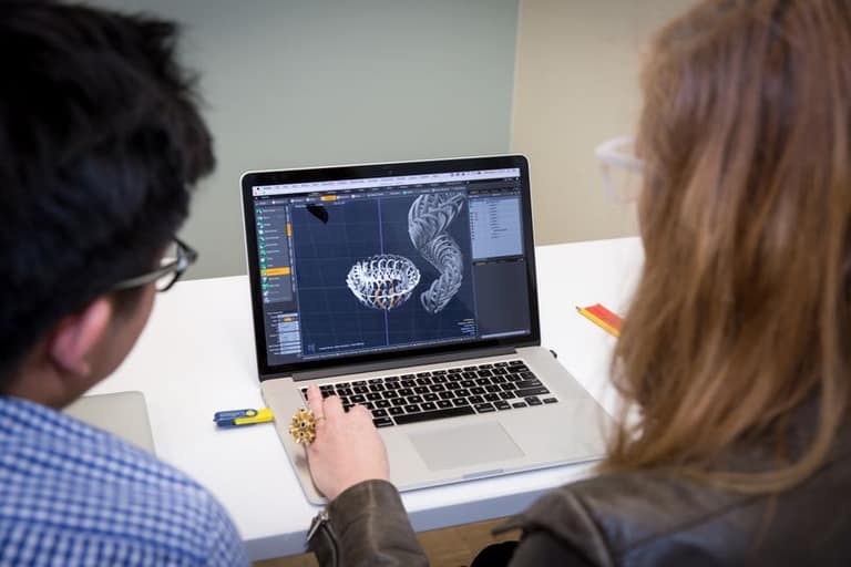 Over-the-shoulder view of people looking at a 3D print design on a screen