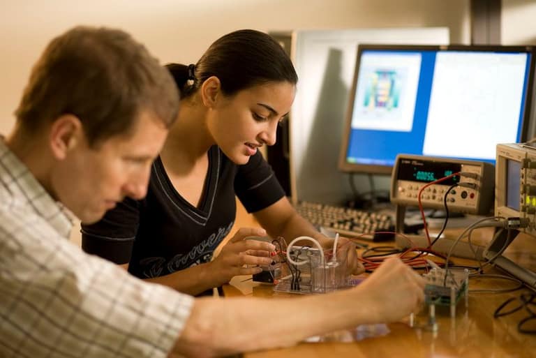 Two students work over circuit boards and equipment